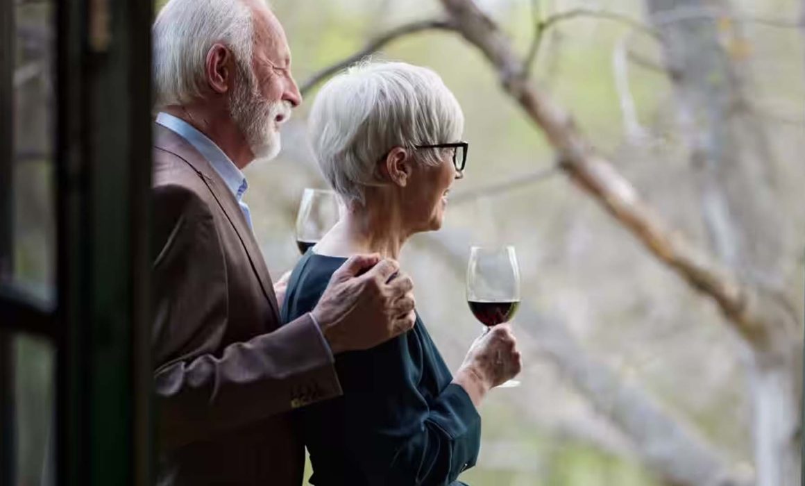 old husband and wife standing in doorway drinking red wine